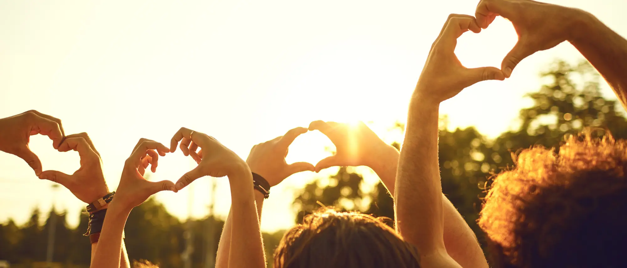 Hands of group friends in the shape of a heart against the sunset.